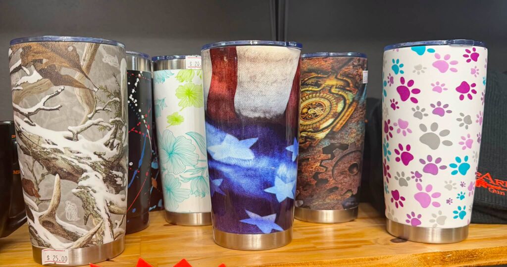 Six insulated tumblers finished in snow camo, paint splatter, floral, American flag, steampunk and paw print hydrographic films